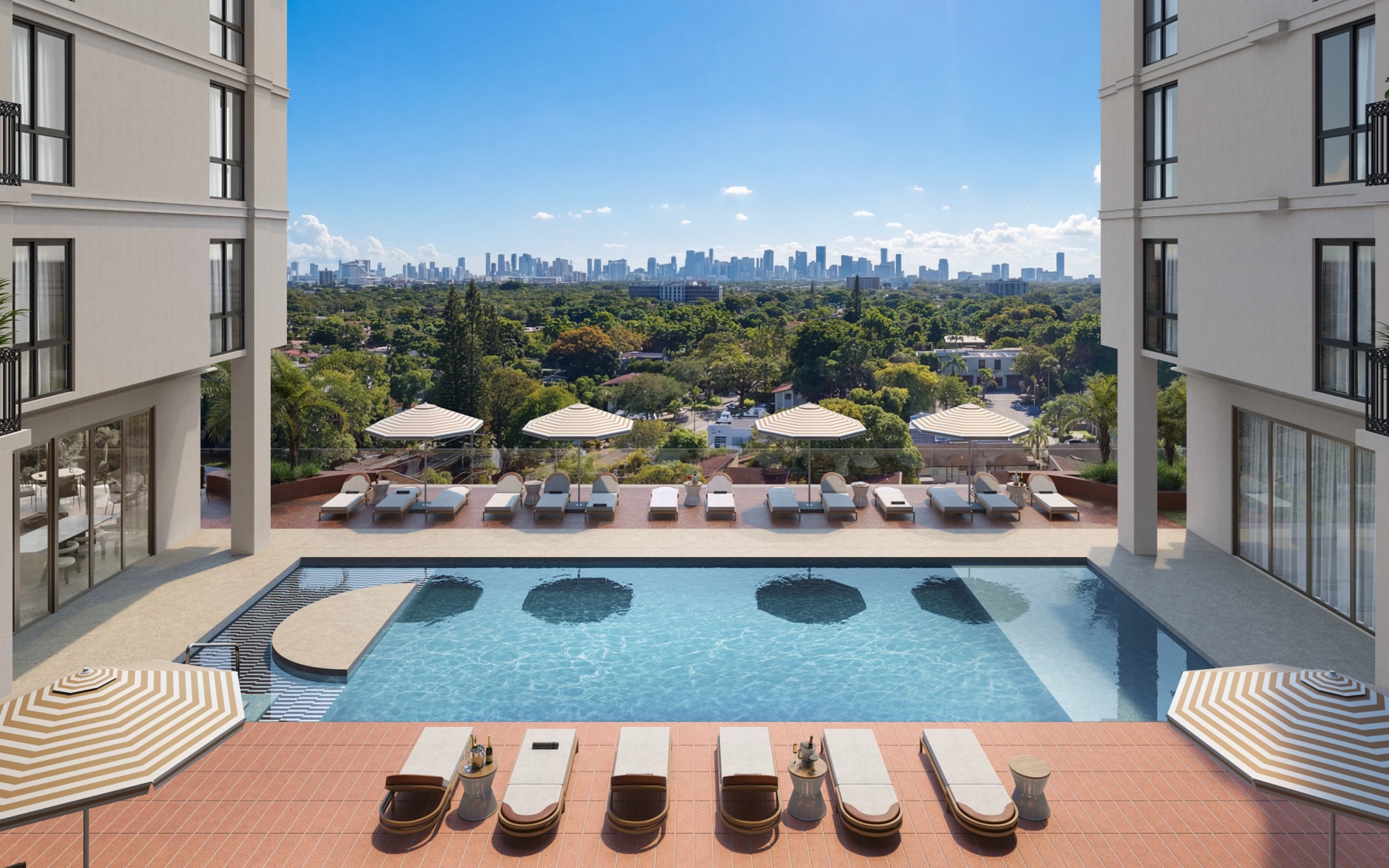 The resort-style pool at Seventeen Gables — integrated in-pool lounging steps, a landscaped sun shelf with striped cabanas, and panoramic views over the Coral Gables canopy to the Miami skyline.